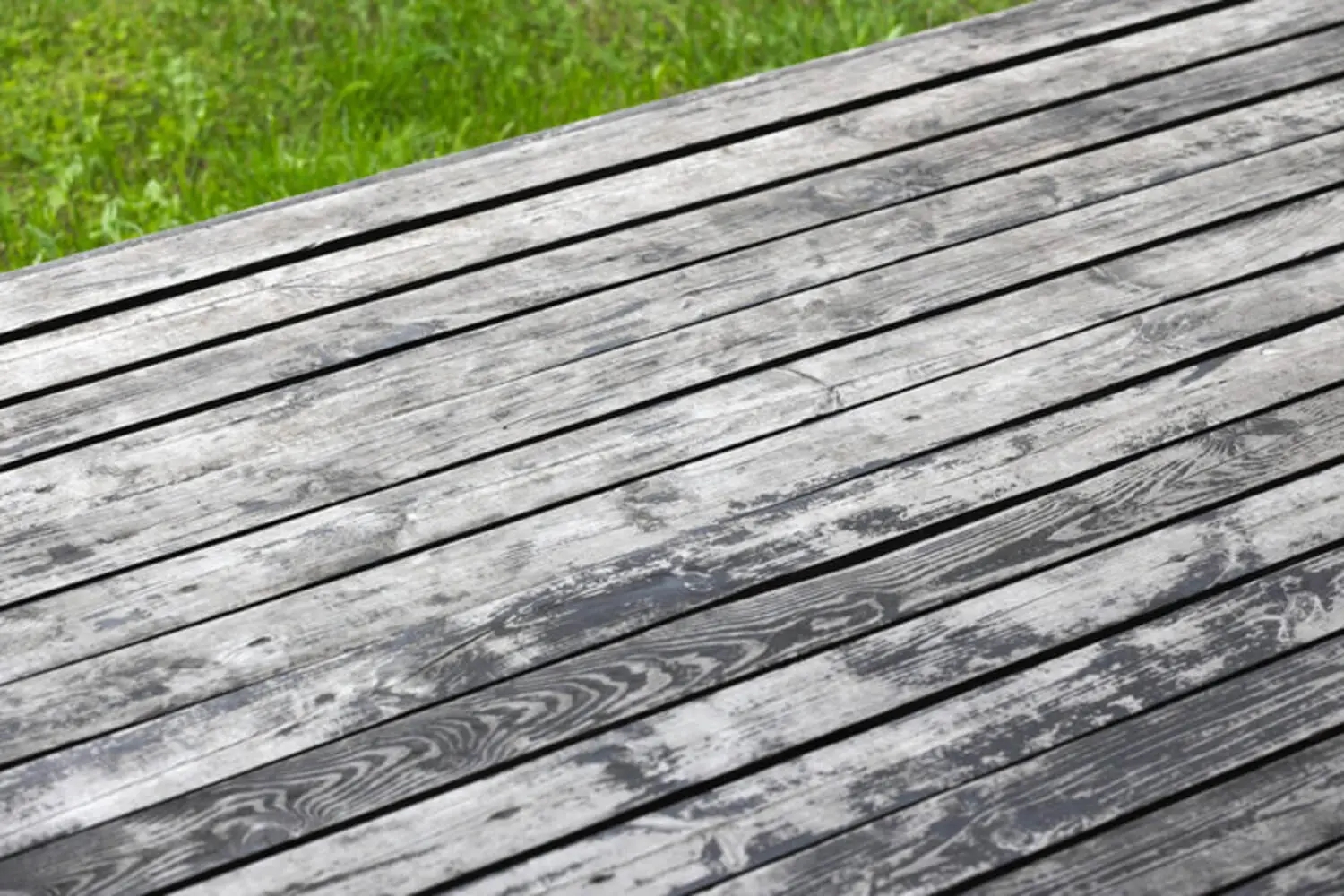 Weathered and greyed wood deck boards showing fading and surface degradation, illustrating how to know if your deck needs staining.