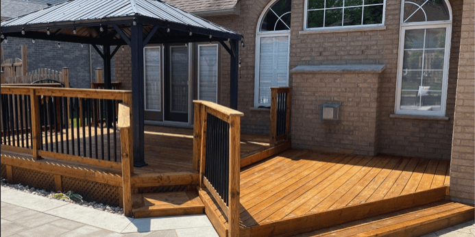 Freshly stained wood deck with black metal railings and wide steps behind a brick home in London, Ontario