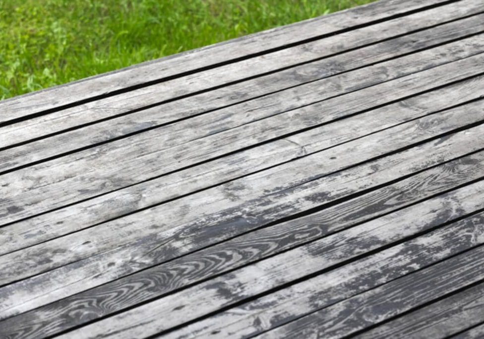 Weathered and greyed wood deck boards showing fading and surface degradation, illustrating how to know if your deck needs staining.
