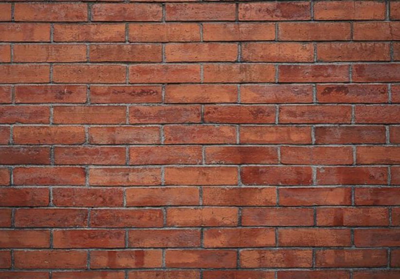 Close-up of a natural red brick exterior wall showing mortar joints and masonry texture, relevant to whether it is better to stain or paint brick.